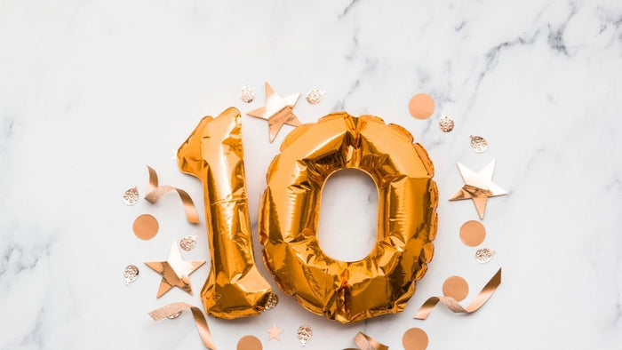 Gold foil balloons shaped as the number 10, surrounded by confetti and paper stars on a marble surface